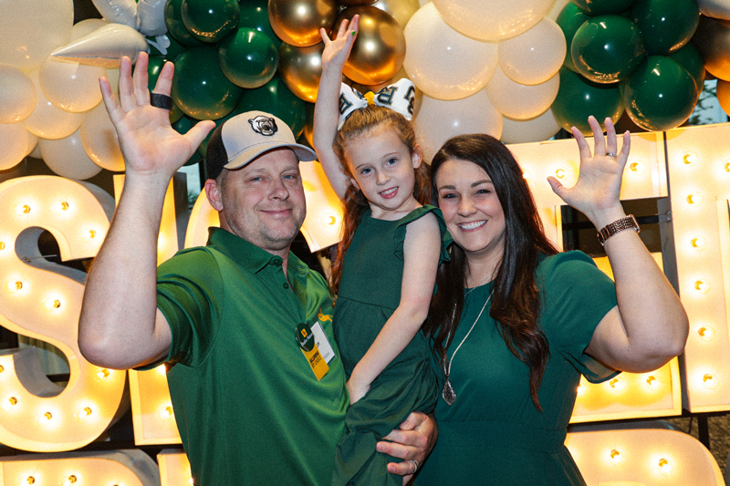 Baylor alumni family doing a Sic 'Em in front of green and gold decor