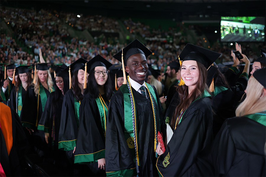 Group of Baylor graduates in cap and gown smiling at the camera